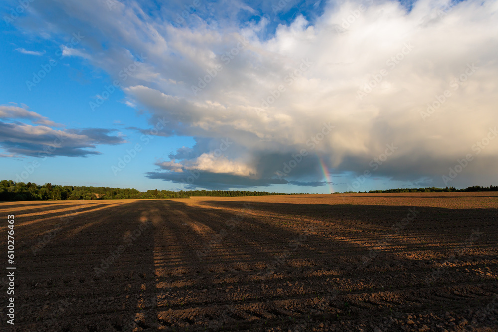 Rainbow over the plowed agricultural field on a background of blue sky