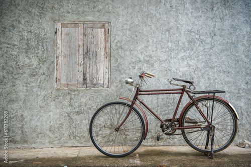 Vintage bicycle on old rustic dirty wall house, many stain on wood wall. Classic bike old bicycle on decay brick wall retro style. Cement loft partition and window background. © BESTIMAGE