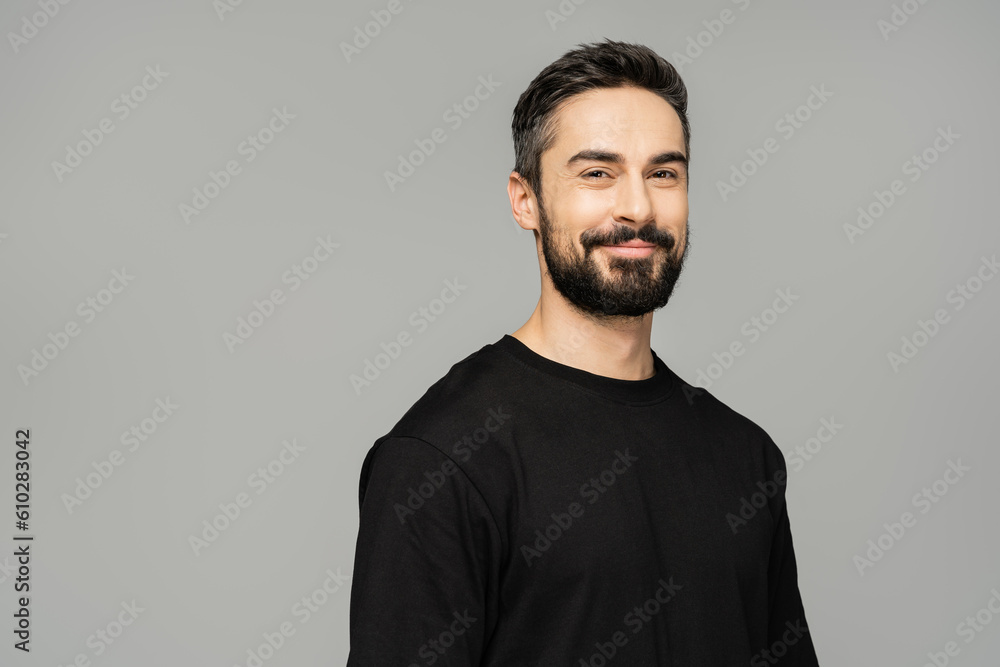 Portrait of cheerful brunette and bearded man in casual black t-shirt smiling at camera while standing isolated on grey, masculine beauty concept, confident and charismatic Portrait of cheerful brunette and bearded man in casual black t-shirt smiling at camera while standing isolated on grey, masculine beauty concept, confident and charismatic