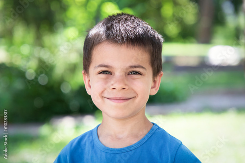 Portrait of little adorable smiling boy in green park on sunny summer day