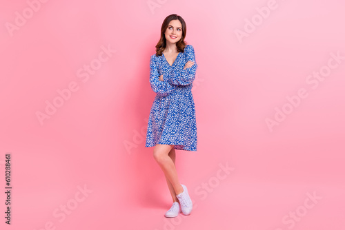 Full length photo of cheerful woman with wavy hairdo wear blue dress arms folded look empty space isolated on pink color background