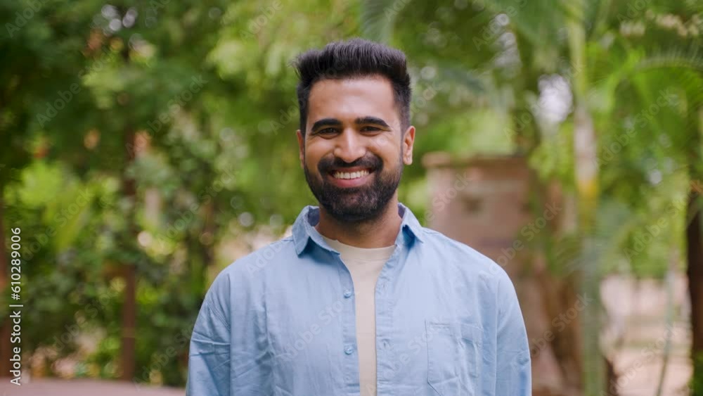 Happy smiling indian man standing by looking at camera at park - concept of successful, confident and positive emotion Happy smiling indian man standing by looking at camera at park - concept of successful, confident and positive emotion