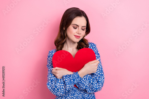 Photo of pretty positive person closed eyes hands hug hold red paper heart isolated on pink color background © deagreez