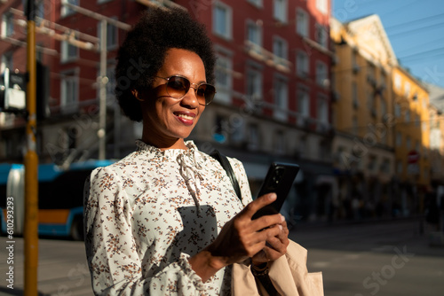 Female tourist walking on a sunny day, using a mobile phone.