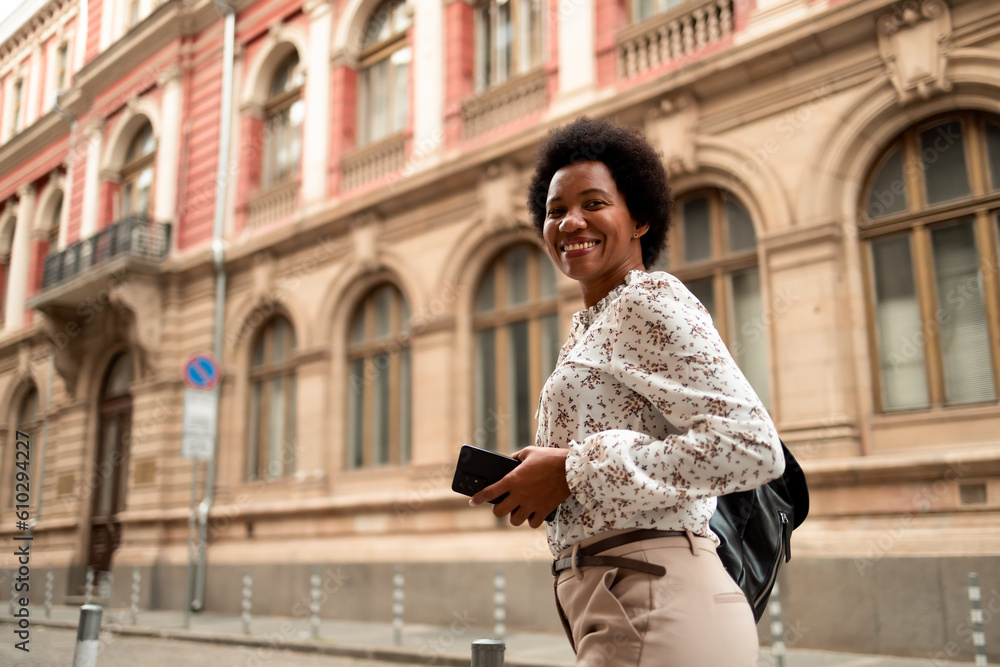 Fototapeta premium Smiling black woman, looking at the camera, walking down the street.
