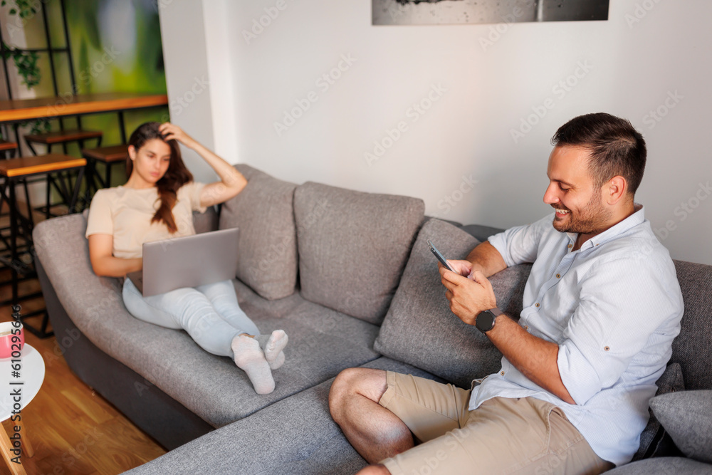 Couple relaxing at home using laptop computer and smart phone