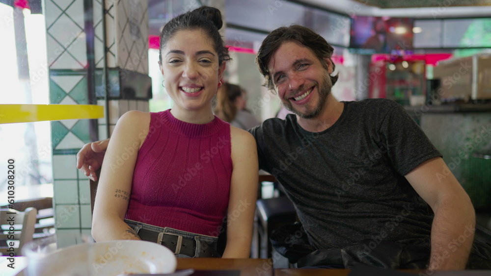 Young man and woman in 30s smiling and laughing while sitting at restaurant place. Happy couple authentic laugh and smile looking at camera Young man and woman in 30s smiling and laughing while sitting at restaurant place. Happy couple authentic laugh and smile looking at camera