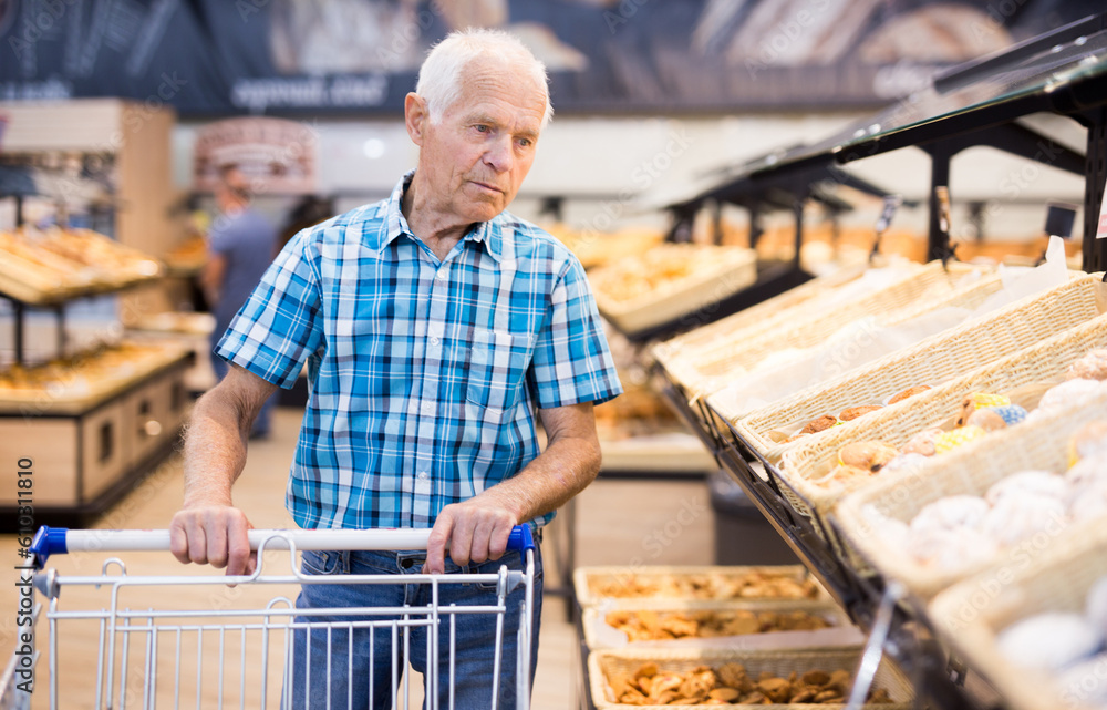 mature senor choosing bread and baking in grocery section of supermarket
