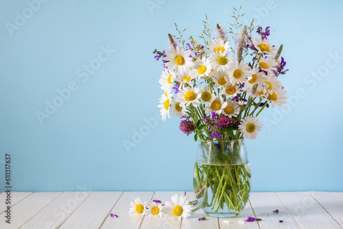 Bouquet of white daisies and other wildflowers in a glass vase on a blue background