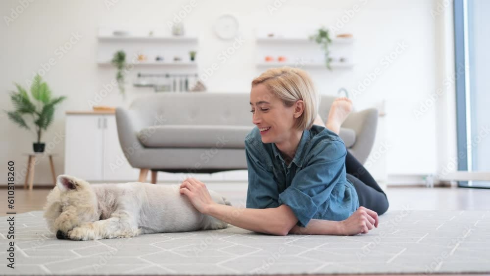 Caring adult female examining dog's coat while lying on room flooring near terrier in spacious house. Stylish young pet owner planning grooming day for her beloved canine companion. Caring adult female examining dog's coat while lying on room flooring near terrier in spacious house. Stylish young pet owner planning grooming day for her beloved canine companion.