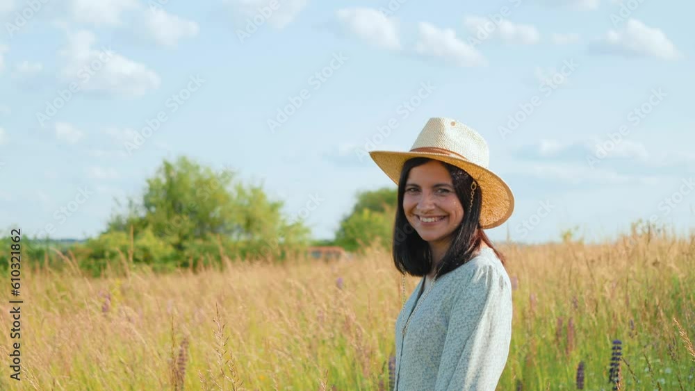 A smiling attractive young adult woman in a dress and a hat on a wild field with flowers, sunny summer A smiling attractive young adult woman in a dress and a hat on a wild field with flowers, sunny summer