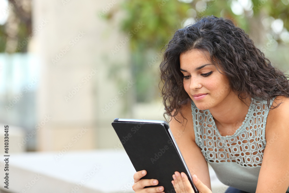 Fototapeta premium Woman using tablet sitting on a bench in a park