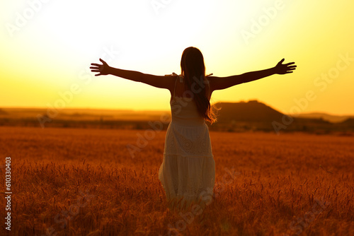Woman silhouette celebrating in a wheat field at sunset