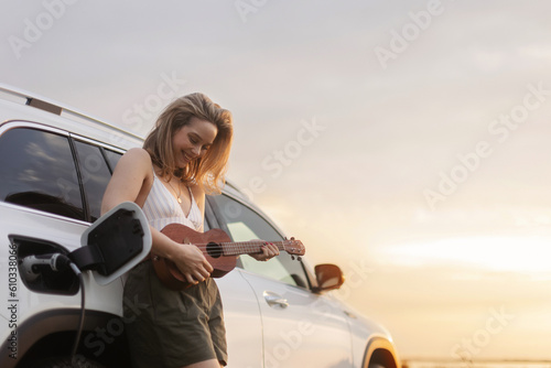 Portrait of young woman leaning on her car,playing on ukulele and enjoying summer time.