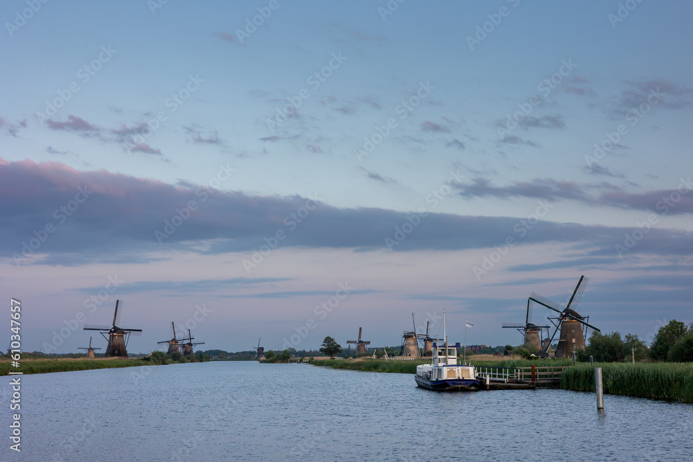 Beautiful wooden windmills at sunset in the Dutch village of Kinderdijk. Windmills run on the wind. The beautiful Dutch canals are filled with water. Beautiful sunset. Beautiful boat on the canal.