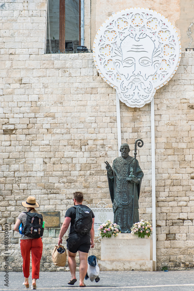 San Nicola, Saint Nicholas bronze statue next to Pontifical Basilica or Church of Saint Nicholas in Bari old town, Puglia, Italy with a couple of tourists walking nearby
