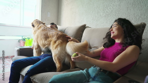 Happy couple with their Dog sitting on couch. Playful Golden Retriever interacting with man and woman. Happiness concept of Pet owners