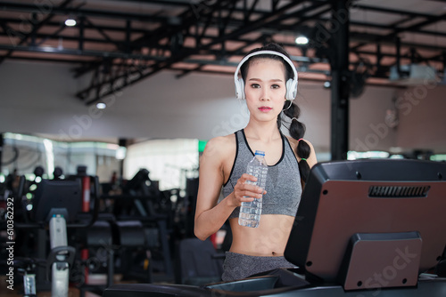 Fitness woman with headphones holding water bottle while resting on treadmill in gym. Healthy lifestyle concept. Woman exercise workout in gym. Gym exercise ,lifestyle and healthy concept.