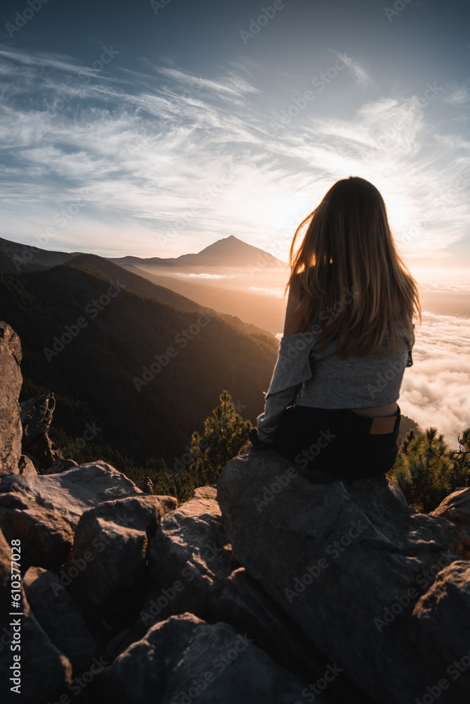 Young woman with long hair sitting on the mountain watching the Teide peak during her tourist trip through Tenerife, in the Canary Islands. 