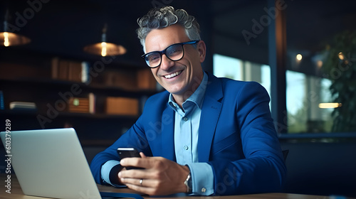 Obraz na płótnie Happy mid aged business man ceo wearing blue suit sitting in office using laptop and smartphone. Mature Businessman professional executive working at desk with laptop. Generative AI w salonie