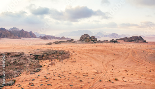 Orange red sand desert  rocky formations and mountains background  overcast sky above  camp tents visible at distance - typical scenery in Wadi Rum  Jordan