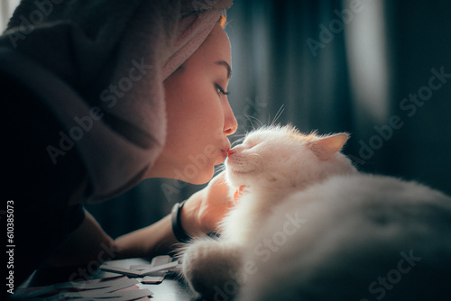 A girl with a towel on her head kisses a white cat on the nose