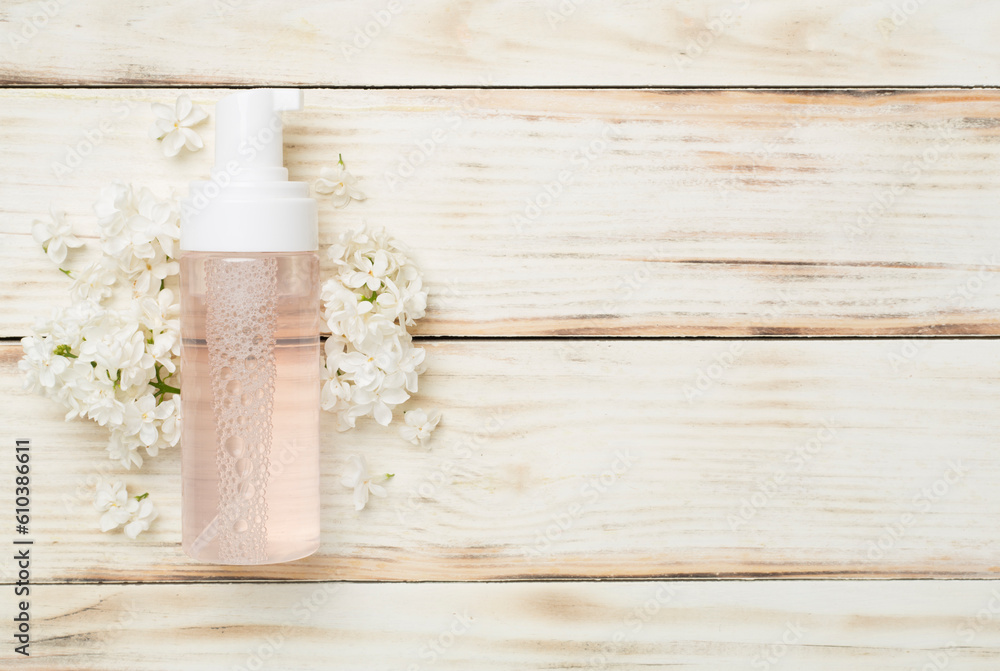 Foaming facial cleanser and with flowers on wooden background, top view Foaming facial cleanser and with flowers on wooden background, top view
