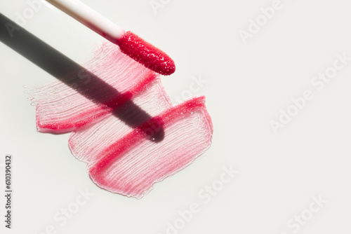 Smears of shining lip gloss and lip gloss brush on white background, hard shadows