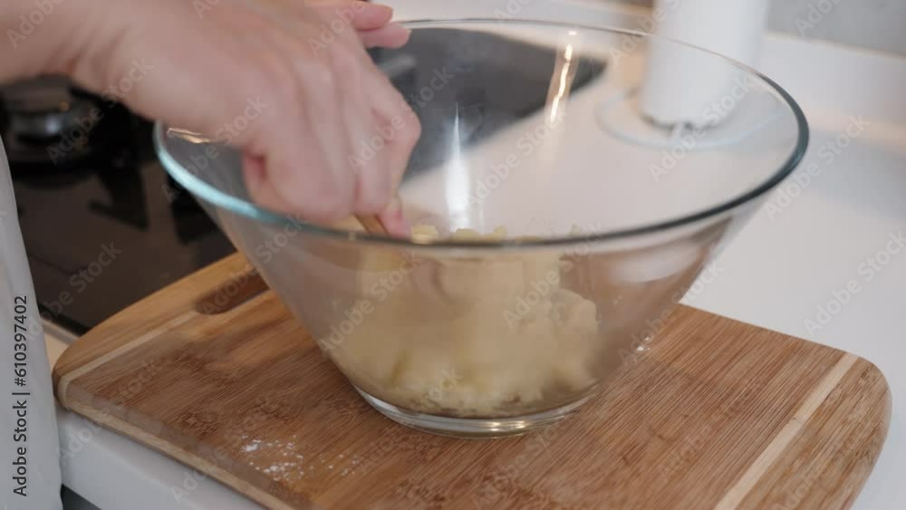 The pastry chef stirs the choux pastry in a large glass bowl, close-up view.