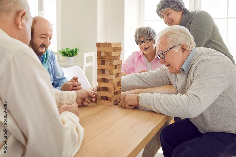 Group of happy senior people having fun and playing board games in community centre or retirement home. Several old men and women sitting around table and playing with wooden block tower together Group of happy senior people having fun and playing board games in community centre or retirement home. Several old men and women sitting around table and playing with wooden block tower together