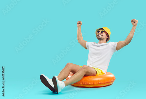 Happy millennial guy in summer hat and sunglasses have fun sit on floating ring get ready for summertime. Funny young man excited about vacation or holidays. Travel and fun concept. photo