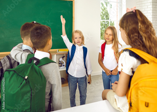Little schoolboy wants to say something and raises his hand while talking to his classmates. Schoolchildren with colorful backpacks on their shoulders are about to go home after school lessons. photo