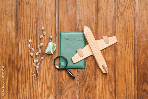 Passport with toy airplane, magnifier, Easter rabbit and willow branches on wooden background