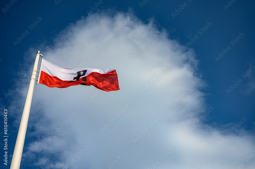Flaga Powstania Warszawskiego, wyraźnie wywieszona na maszcie, symbolizująca wytrwałość i narodową dumę na tle jasnego nieba. - obrazy, fototapety, plakaty 