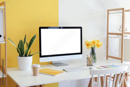 Modern PC, beautiful narcissus flowers, houseplant, coffee, notebook and paint color palettes on table near color wall © Pixel-Shot