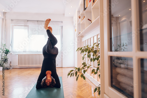 Fototapeta Dark haired girl doing headstand with eagle legs while balancing and enjoying