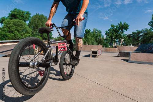 Cropped picture of a tattooed man doing a 360 rotation on his bmx in a skate park.
