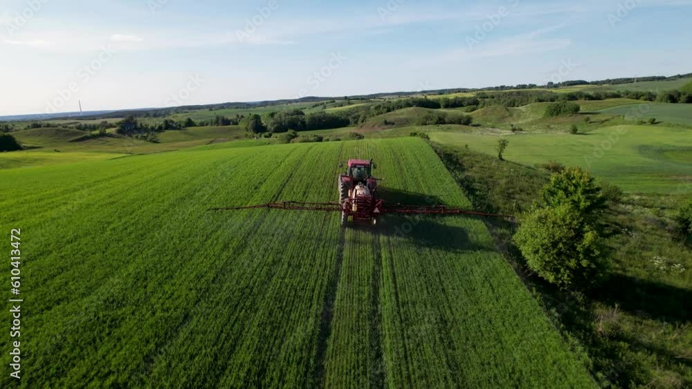 Aerial establishing view of Spraying a green wheat field by tractor. The farming tractor spraying on field with sprayer, herbicides and pesticides. Industrial machine fertilizing a field Aerial establishing view of Spraying a green wheat field by tractor. The farming tractor spraying on field with sprayer, herbicides and pesticides. Industrial machine fertilizing a field
