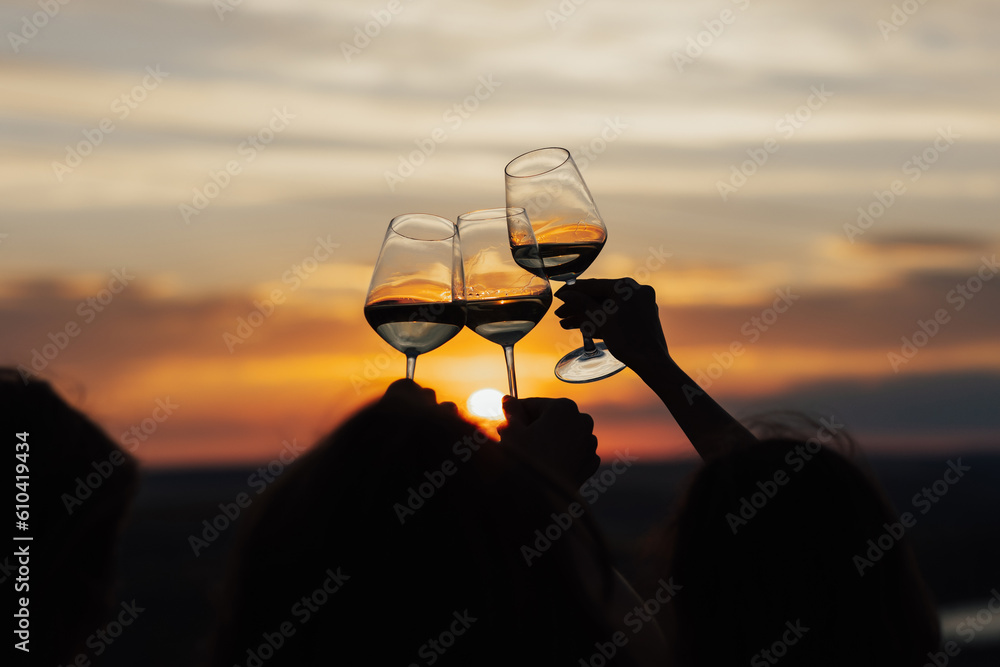 Close-up of hands cheers with glasses of wine at amazing sunset. Clinking glasses at sunset.