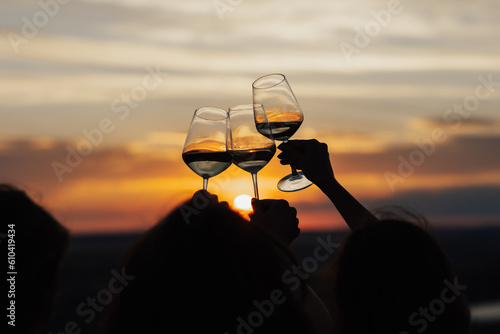 Obraz na płótnie Close-up of hands cheers with glasses of wine at amazing sunset. Clinking glasses at sunset. w salonie