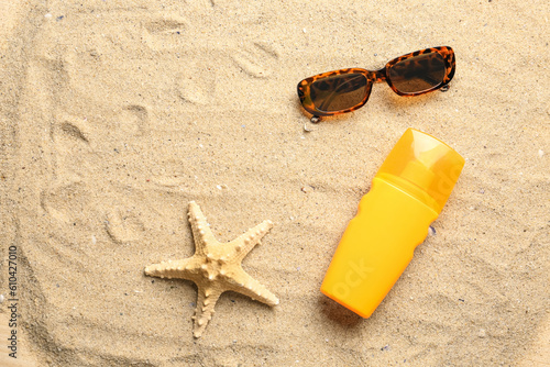 Bottle of sunscreen cream with sunglasses and starfish on sand