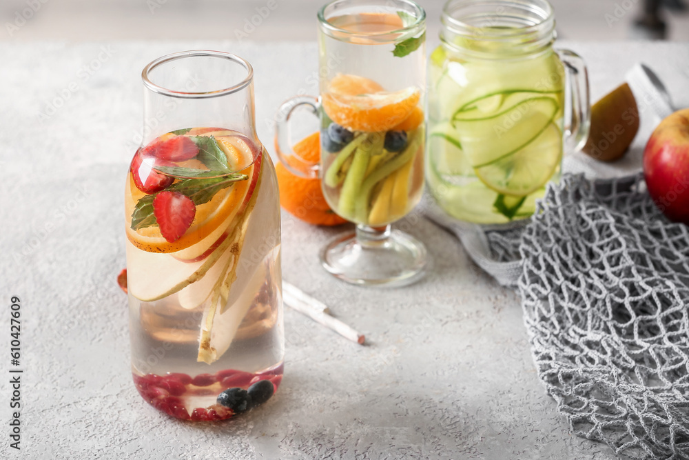 Fototapeta premium Glass, mason jar and bottle of infused water with different sliced fruits on grey table