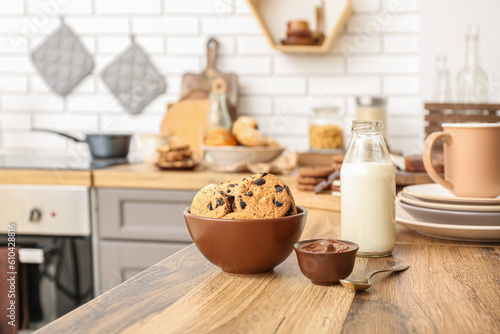 Bowl with cookies, bottle of milk and chocolate cream on wooden table in kitchen