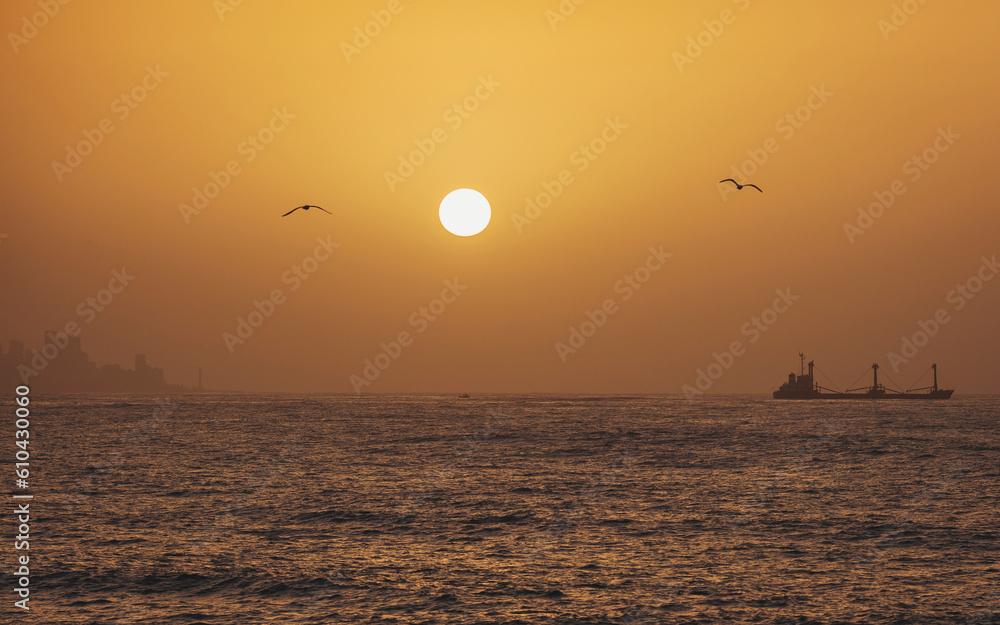 Distant merchant ship sailing in an open mediterranean sea on sunset. Tanker in the sea. Beautiful sunrise over the sea in Beirut, Lebanon. Cargo ships floating on rippling sea in sunset.