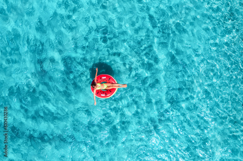 Aerial view of a woman swimming with red swim ring in blue sea at sunrise in summer. Tropical landscape with girl, ocean with azure water, sandy beach. Top view. Vacation in Sardinia island, Italy