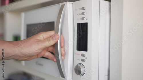 Video of an unrecognizable man's hand placing his cup of tea or coffee inside the microwave activating it to heat it up. photo