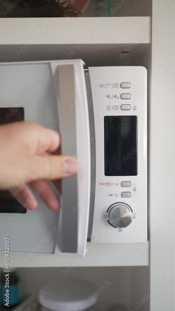 Vertical front video of a hand placing a cup to heat in the microwave, pressing the operation button twice to start heating. Vertical front video of a hand placing a cup to heat in the microwave, pressing the operation button twice to start heating.