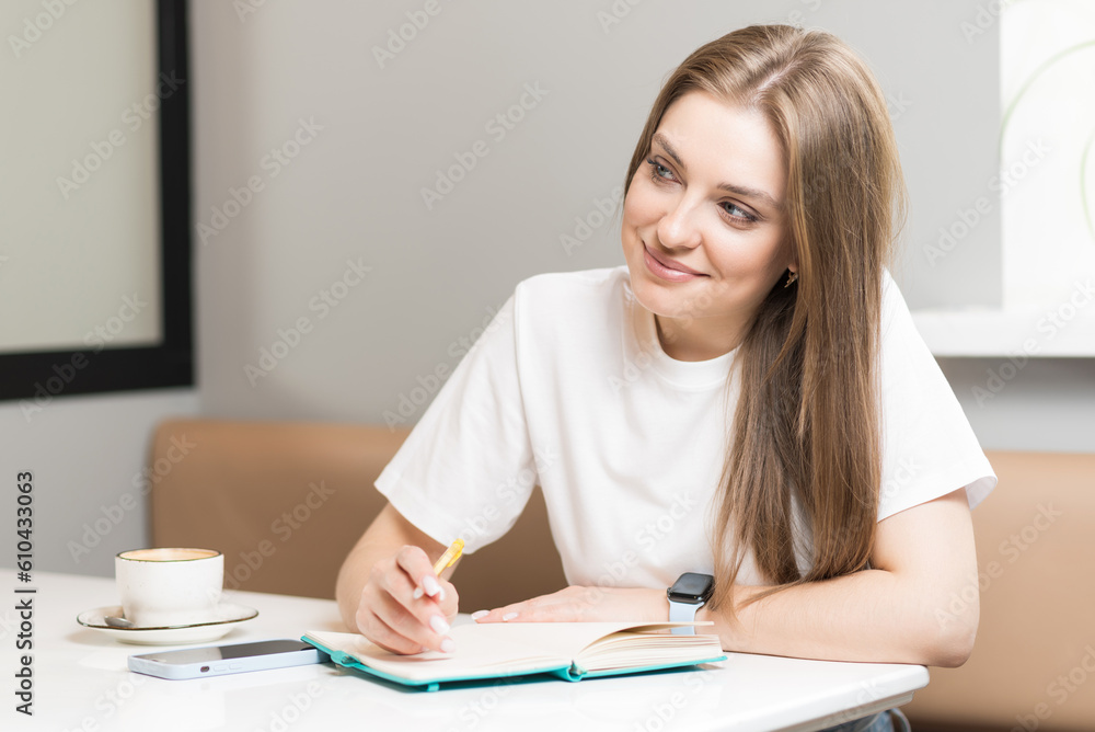 A girl writer is writing a book in a notebook in a cafe.