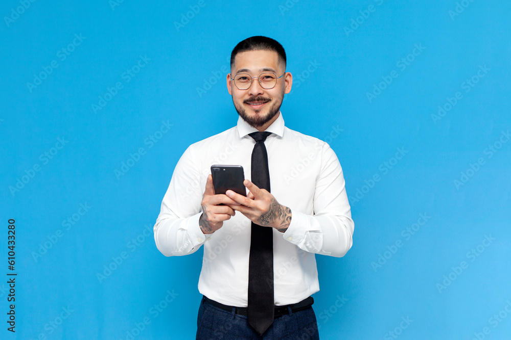 successful Asian businessman in white shirt and tie uses smartphone on blue isolated background successful Asian businessman in white shirt and tie uses smartphone on blue isolated background