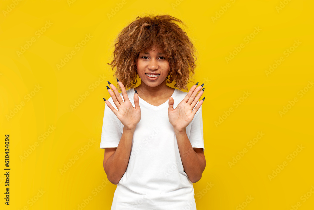young curly american girl with braces shows palms on yellow isolated background young curly american girl with braces shows palms on yellow isolated background